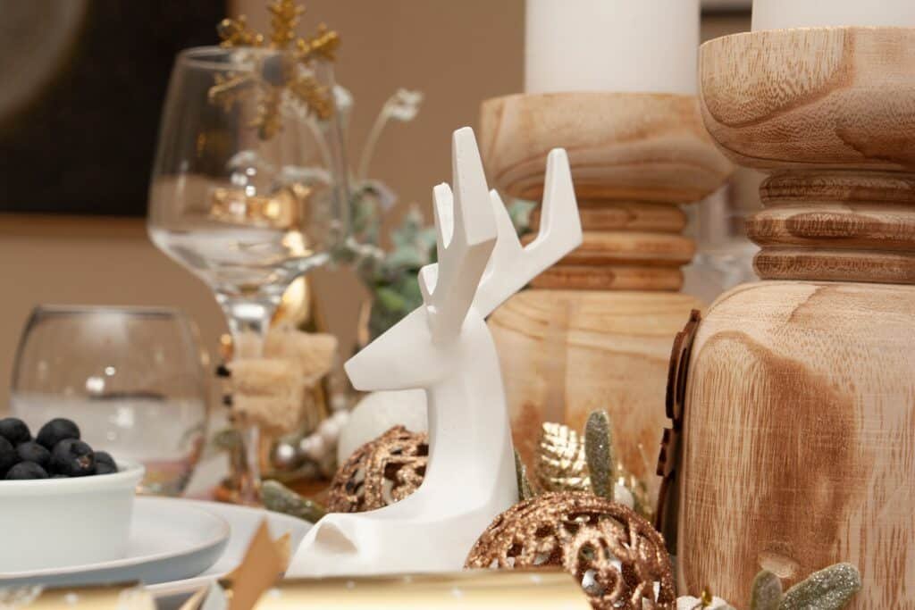 Reno decorativo blanco junto a portavelas de madera, velas blancas y adornos metálicos en una mesa navideña.